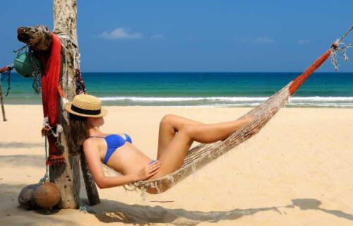 Picture of a woman in a two piece blue bikini, lying in a hammock on the beach in Costa Rica, and happy with her dental work at Premier Holistic Dental in Costa Rica