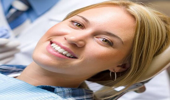 Portrait picture of a smiling woman with long blonde hair, sitting in a dental chair, looking at the camera and showing her happiness with the dental inlays and onlays she had in Costa Rica.