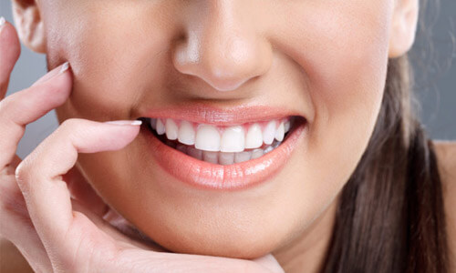 Close-up picture of a smiling young woman, holding her hand to her face to show perfect white teeth, and happy with her Holistic dental extractions treatment at Premier Holistic Dental in Costa Rica.