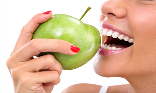 Close-up picture of a smiling young woman biting into a green apple after having a Holistic dental whitening treatment at Premier Holistic Dental in Costa Rica.